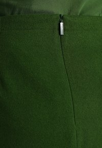 Falda de fieltro verde con una textura suave, que presenta un cierre de cremallera oculto y una forma limpia y entallada.