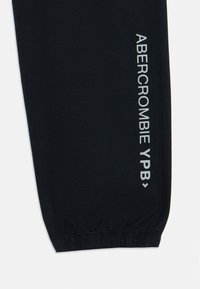 Black athletic jogger featuring elastic cuffs and a side print in silver reading "ABERCROMBIE YPB." Made of smooth, stretchy fabric.