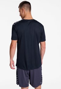 Camiseta atlética negra de manga corta, con textura suave y dobladillo redondeado. Cuenta con un patrón de cheurón reflectante en los hombros.