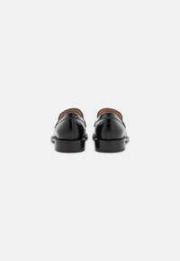 Mocasines de cuero negro con textura de cocodrilo grabada, punta redondeada, tacón bajo y un forro interior suave. Diseño minimalista sin herrajes visibles.