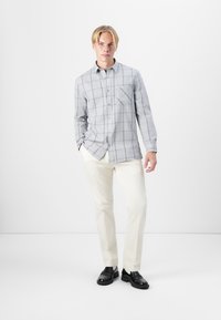 Gray checkered shirt with a pocket, button-down design, worn with cream-colored pants and black shoes on a plain background.