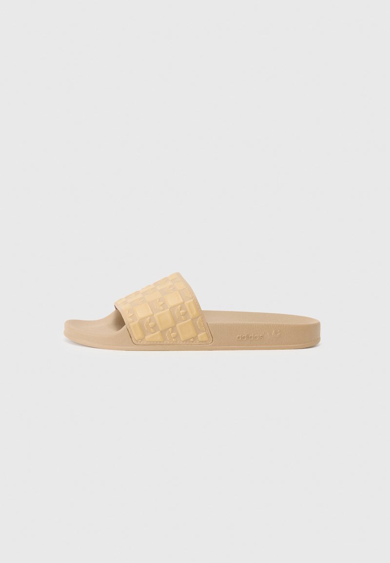 Sandal s ravnom đonom u bež plastici, s teksturiranim remenom s šahovskim uzorkom i utisnutim logotipom. Opušteni dizajn s otvorenim prstima.