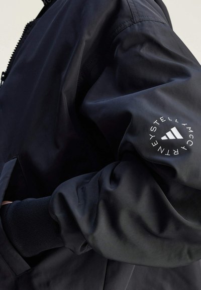 Černá bomber bunda s hladkým, matným povrchem. Má žebrované manžety a bílé logo na rukávu. Minimalistický design bez viditelných vzorů.