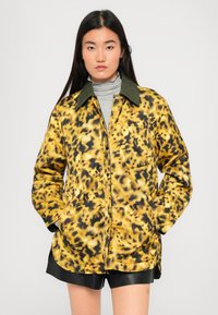 Giacca a stampa leopardata gialla e nera, con colletto verde, chiusura a bottoni e tasche laterali. Tessuto morbido con una vestibilità comoda.