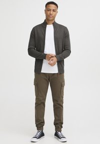 Dunkelgrauer Reißverschluss-Pullover über einem weißen T-Shirt, kombiniert mit olivfarbenen Cargo-Hosen und schwarzen Sneakers. Slim-Fit mit gerippten Bündchen.