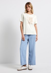 T-shirt en coton de couleur claire à manches courtes avec un imprimé graphique en beige doux. Assorti à un pantalon large en denim bleu clair, ample.