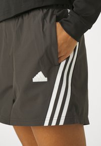 Shorts desportivos pretos com um cós elástico, bolsos laterais, padrão de três riscas brancas e um logotipo branco da Adidas no lado esquerdo.