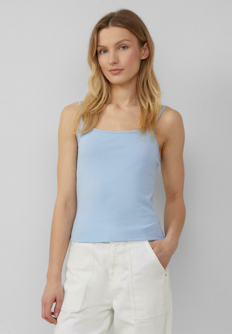 Top senza maniche di colore azzurro chiaro con scollatura quadrata. Realizzato in tessuto morbido, presenta una silhouette aderente e una texture liscia. Abbinato a pantaloni bianchi.