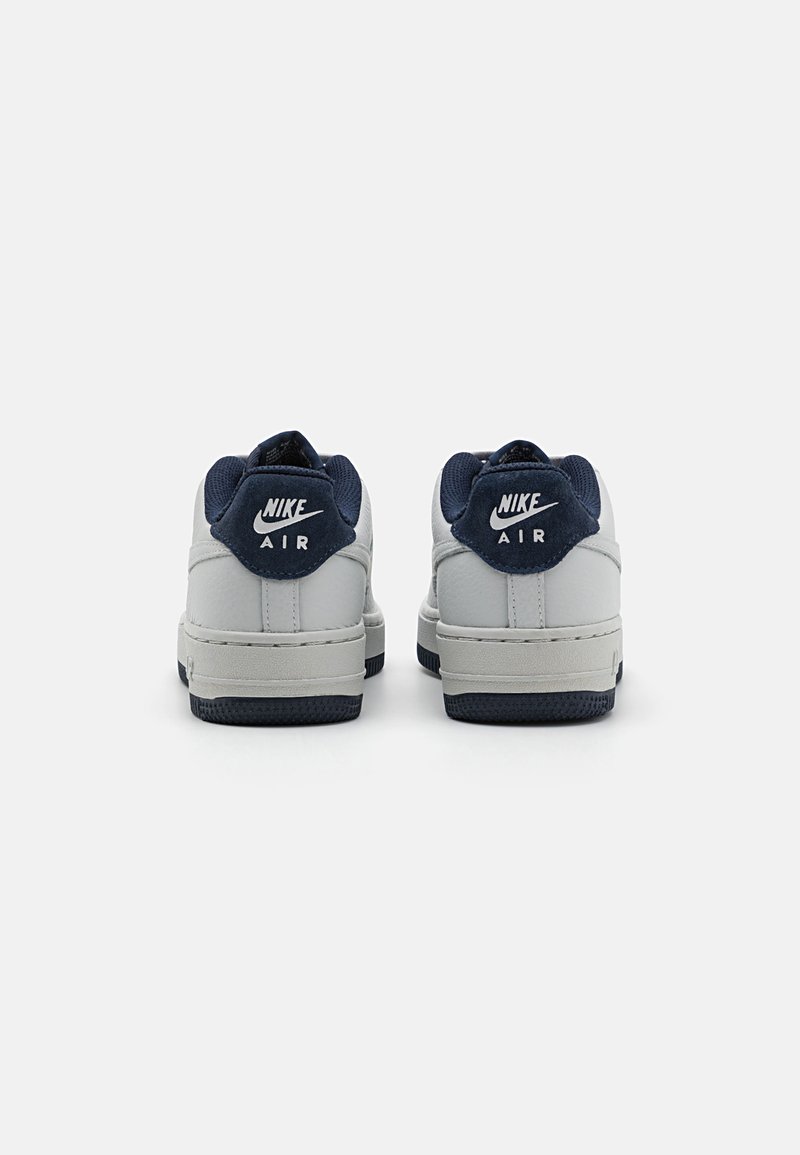 Zapatillas blancas y marino con cuero texturizado, que presentan una punta redonda, suelas de goma y el logotipo "Nike Air" en el talón.