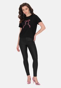Sort t-shirt med en pink glimmergrafik i form af en sløjfe, parret med tætsiddende sorte bukser og blanke pink højhælede sko.