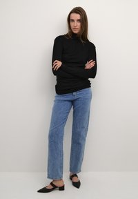 Maglione nero a maniche lunghe con collo a imbuto, a taglio aderente, abbinato a jeans dritti a vita alta di un blu chiaro e décolleté slingback neri con punta a punta.