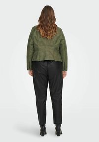 Chaqueta de ante verde con una cintura ajustada y mangas largas, combinada con pantalones de cuero negros. La chaqueta presenta una textura suave y detalles con cremallera.