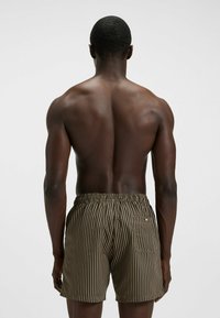 Gestreifte Badehosen in Braun und Schwarz mit einem elastischen Taillenbund und einer Gesäßtasche. Der Stoff wirkt leicht und glatt.