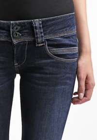 Mörkblå denimjeans med en åtsittande design, synlig sömnad och två framfickor. Har en tvåknappars knäppning och en jämn textur.