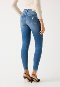 Džínsy skinny vo stredne modrej farbe, s vysokým pásom, dvoma zadnými vreckami s trojuholníkovým logom a slim fit až po členky.