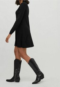 Svart långärmad klänning med utsvängd kjol, i kombination med knähöga svarta läderstövlar med spetsig tå och siddragkedjedetalj.