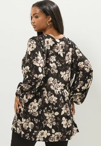 Tunic nera floreale con maniche a sbuffo lunghe, vita cinchata e orlo morbido. Il design presenta grandi rose rosa chiaro e foglie verdi.