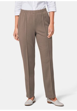 Frau trägt taupe gerade geschnittene Hose mit elastischem Bund, kombiniert mit weißen Loafern und einem weißen Hemd mit Knöpfen.