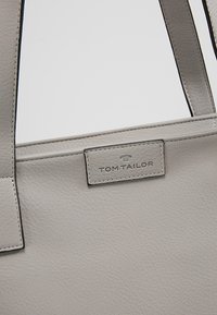Sac fourre-tout en cuir gris avec une surface texturée, comportant un patch logo rectangulaire portant l'inscription "TOM TAILOR" et de élégantes poignées droites.