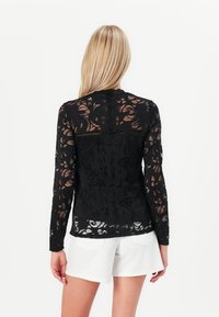 Black long-sleeve lace top featuring floral patterns, a round neck, and a semi-sheer design, paired with white shorts.