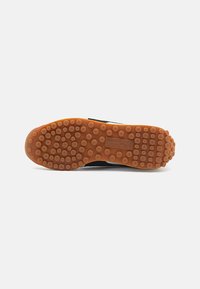 Suela de zapatilla deportiva negra con goma texturizada que presenta agarraderas circulares, base color goma y un logo en la zona del talón.