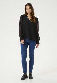 Czarna bluzka w kropki z dekoltem w szpic i bufiastymi, przezroczystymi rękawami, zestawiona z niebieskimi skinny jeansami i czarnymi loafersami.