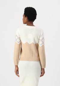 Maglione lavorato a maglia con un design a blocchi di colore crema e beige, con orlo e maniche a coste. MotivI decorativi simili all'uncinetto sulle spalle.