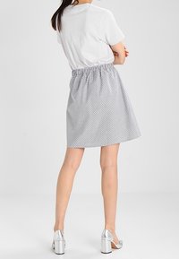 Jupe à taille élastique avec un motif à rayures gris et blanc, longueur au-dessus du genou, associée à un t-shirt blanc ajusté et des sandales à talons argentés.