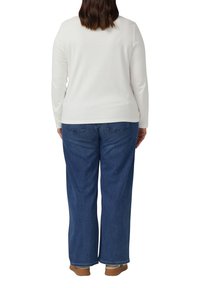 Langärmliges weißes Oberteil mit rundem Ausschnitt, kombiniert mit weit geschnittenen dunkelblauen Jeans. Verfügt über einen lässigen Schnitt und ein einfaches Design.