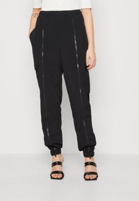 Svarta, lätta joggerbyxor med elastisk midja, blixtlåsfickor fram och elastiska fållar för en smal passform. Sidofickor ingår.