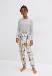 Maglietta grigia a maniche lunghe con design di pinguino; pantaloni del pigiama a quadri in beige, marrone e grigio; polsini elastici alle caviglie.