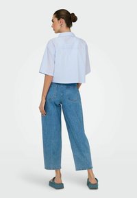 Camisa de rayas recortada en azul claro y blanco, combinada con jeans de mezclilla de pierna ancha y cintura alta. Tejido suave con detalles de costura visibles.