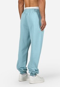 Šviesiai mėlynos sportinės kelnės su reguliuojamu juosmeniu ir šonkačių rankovėmis, pagamintos iš minkštos medžiagos. Dėvimos su baltomis sportinėmis bateliais.