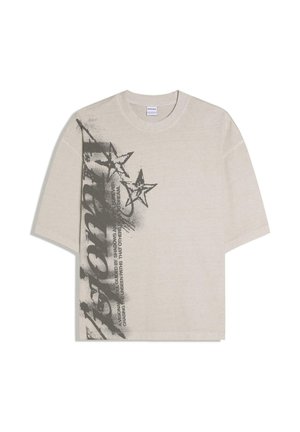 Béžové tričko s krátkym rukávom s čiernymi graffiti-hviezdami a tučným vertikálnym textom na ľavej strane.