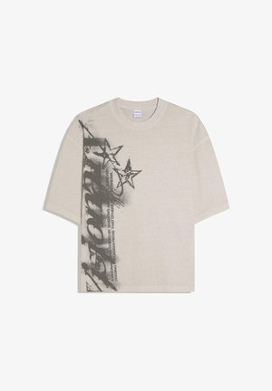 Béžové tričko s krátkym rukávom s čiernymi graffiti-hviezdami a tučným vertikálnym textom na ľavej strane.