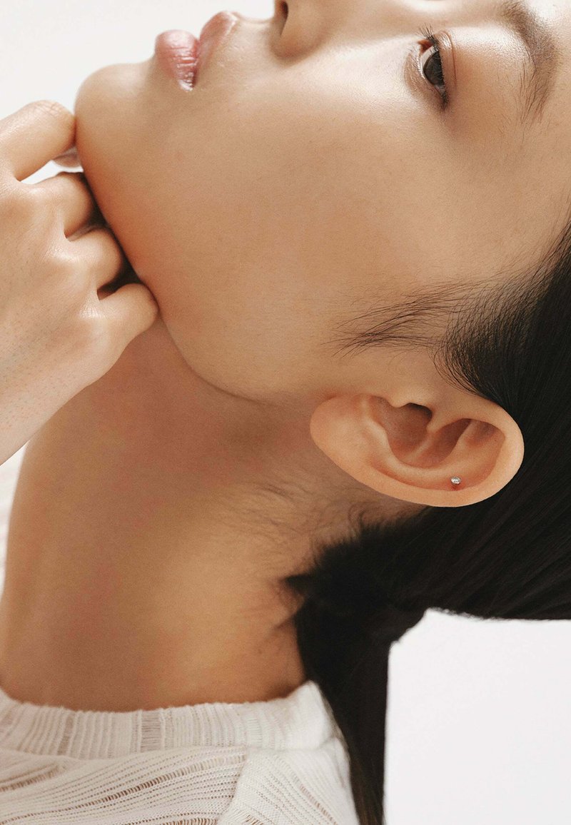 Pendiente de plata en un primer plano de la oreja de un modelo. La piel es suave, con el cabello oscuro recogido que acentúa el pendiente.
