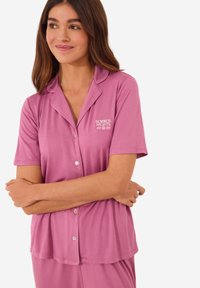 Korte mouwen, roze pyjama set met een knoopsluiting bovenaan. Bevat een klein geborduurd "ZOMERNACHTEN" logo en heeft een gladde, zachte textuur.
