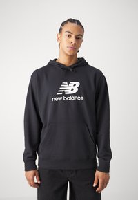 Fekete kapucnis pulcsi puha anyagból, elülső zsebbel, húzózsinóros kapucnival és nagy fehér "New Balance" logóval a mellkasán.