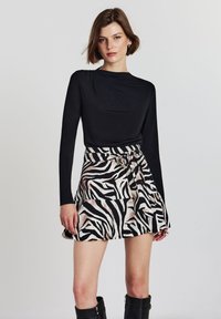 Schwarzes Langarmoberteil kombiniert mit einem Zebramuster-Rock mit gebundenem Bund, geschichteten Rüschen und schwarzen kniehohen Stiefeln. Glatte Textur.