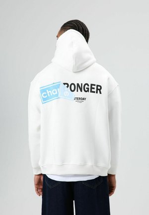 Witte oversized hoodie met een grote zwarte tekst "STRONGER" en een blauw grafisch element op de achterkant. Glad stof en een ontspannen pasvorm.