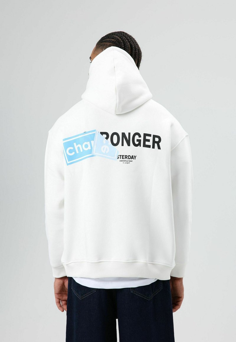 Witte oversized hoodie met een grote zwarte tekst "STRONGER" en een blauw grafisch element op de achterkant. Glad stof en een ontspannen pasvorm.