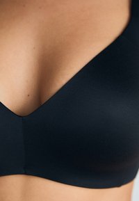 Black seamless bra with a V-shaped neckline, made of smooth fabric. Features a simple design, no embellishments or hardware visible.