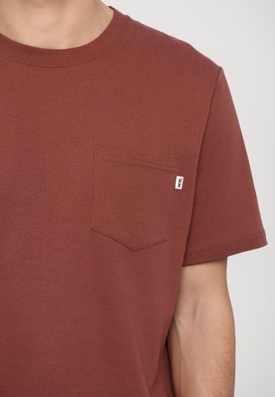 T-shirt en coton bordeaux avec col rond, manches courtes et une poche poitrine à l'avant avec une petite étiquette. Texture lisse, design décontracté.