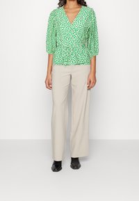 Blouse péplum verte à petit imprimé floral, décolleté en V profond et manches bouffantes, associée à un pantalon beige à jambes larges et des bottines noires.
