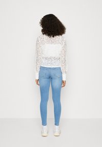 Top bianco in pizzo con maniche lunghe abbinato a jeans skinny blu chiaro. Le sneakers completano l'outfit, presentando un motivo in pizzo testurizzato.