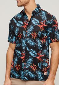 Camisa de manga corta negra con un vibrante patrón de hojas y flores tropicales en tonos azules y rojos, con cuello abotonado y botones negros.