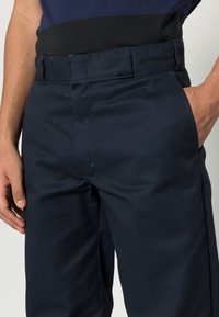 Navy blue trousers made of a smooth fabric, featuring a classic fit, side pockets, and a wide elastic waistband.