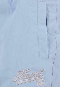 Gaiši zili šorti no teksturēta auduma, ar sānu kabatu un izteiksmīgu balto izšuvumu ar "Kani" un "89" detaļām.