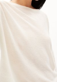 Ljust beige tröja i mjukt, texturerat tyg. Har en lös passform och vid nackringning, med ett ribbat mönster över hela.