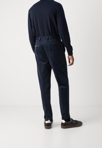 Navy kordflorsebyxor med rak bendesign, sid- och bakfickor, i kombination med svarta sneakers med vita accenter.